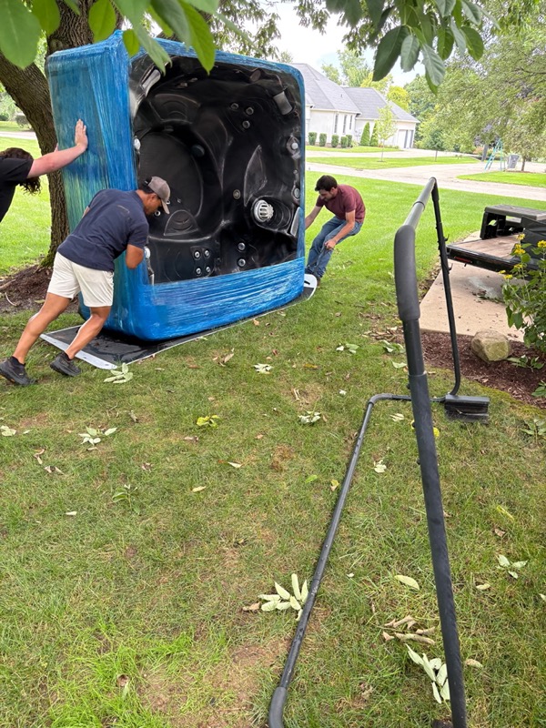 Crew moving a wrapped hot tub across a lawn